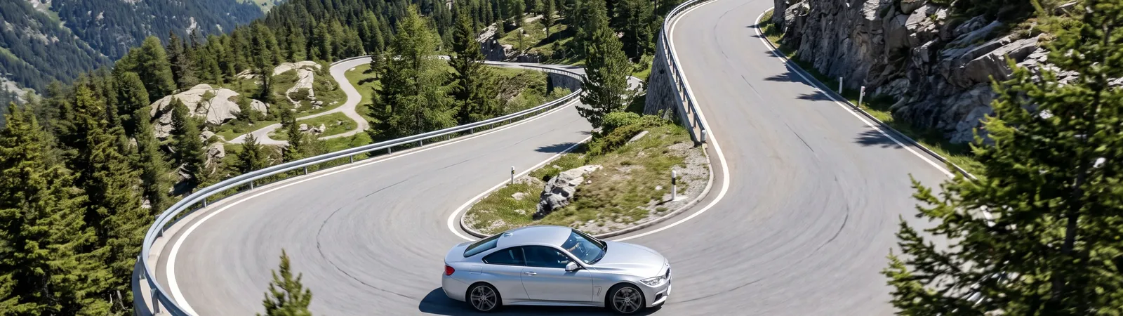 Silberner Sportwagen in einer Kehre einer sonnigen Bergstraße